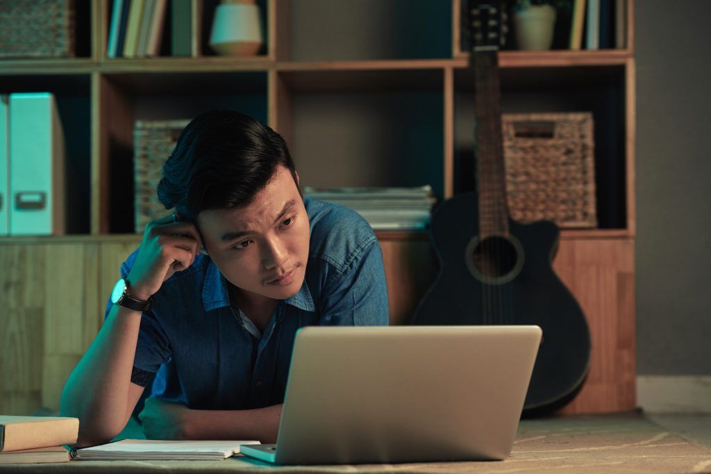 Asian university student lying on floor and reading a book on laptop screen