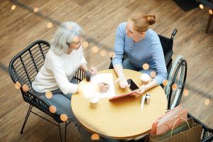 Young disabled woman pointing at digital tablet and explaining something to senior woman while she filling some document in cafe