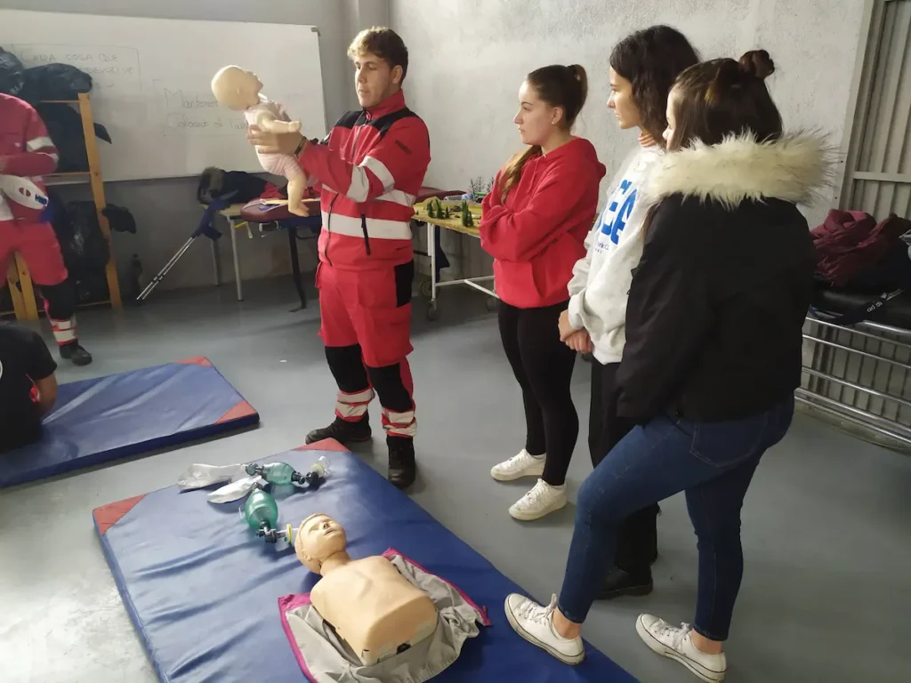 Instructor enseñando RCP con un maniquí de bebé a tres alumnas en un aula.